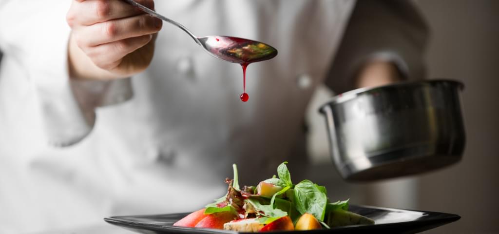 A chef adding a sauce drizzle to a salad.